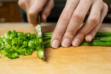 Obraz na płótnie Canvas Women's hands cut green onions with a knife on a wooden Board close up