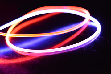 A wire with orange and blue light, a light guide wire with different light transmission, light spectrum, and light effects located in a chaotic state with light reflection on a black glossy background
