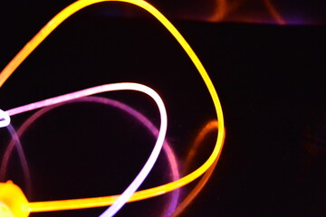 Yellow and blue light wire, a light guide wire with different light transmission, light spectrum, and light effects located in a chaotic state with light reflection on a black glossy background.