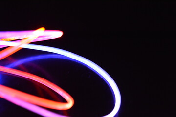 Orange and blue light wire, a light guide wire with different light transmission, light spectrum, and light effects located in a chaotic state with light reflection on a black glossy background.