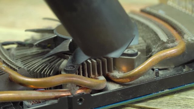 A male hand with a brush and a vacuum cleaner cleans the cooler from the video card close-up. Dust on a processor cooler close-up of a computer graphics card on a wooden table.