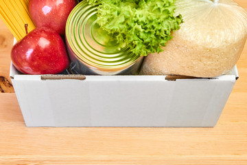 Donation box with vegetables, zucchini, salad, fruits, apples, olive oil, rice, pasta and tin on a wooden background