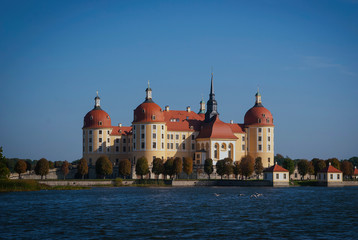 Fototapeta na wymiar View of Moritzburg Castle, Germany from a distance. Beautiful yellow castle with a red roof against a blue sky on the river bank on a sunny day.