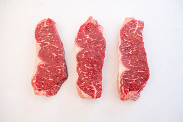 Three Raw Beef Strip Loins Steak Side by Side on a White Quartz Kitchen Countertop