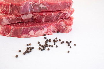 Raw Beef Strip Loins Steak and Some Black Pepper Corns on a White Quartz Kitchen Countertop