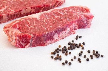 Raw Beef Strip Loins Steak and Some Black Pepper Corns on a White Quartz Kitchen Countertop