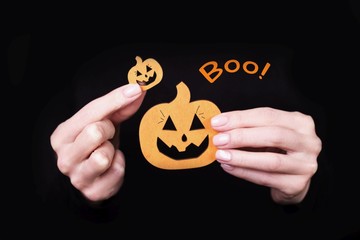 Female hands holding funny little pumpkins on black background. Halloween card with Boo inscription