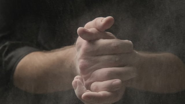 Chef clapping hands covered in flour in slow motion. Baker working with dough and flour at black background. Close-up of man hands