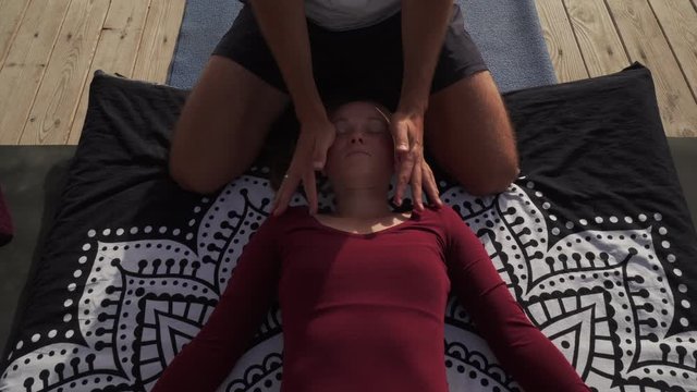 Massagiste doing head thai yoga massage to woman outside at sunset