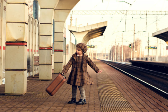 Beautiful charming little girl waiting for train at station holding luggage