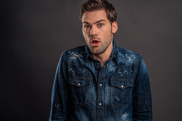 Surprised man. Surprised young man in denim shirt looking at camera and keeping mouth open while standing against grey background