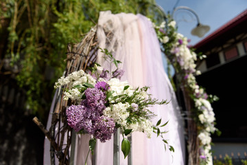 Round wedding arch decorated with tree branches, lilac flowers and other spring flowers. Stylish and contemporary decoration of a wedding ceremony outdoors.