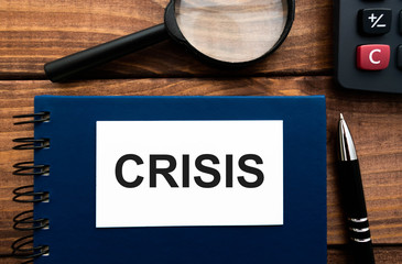 Word CRISIS written on a notebook with calculator and magnifying glass on wooden backround.