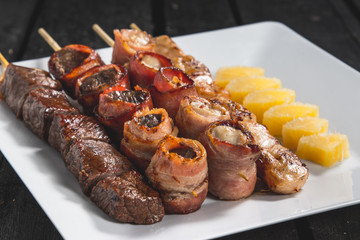 Espetinhos assados de carne, medalhão de carne e frango com bacon, queijo e mandioca cozida servido em prato no boteco