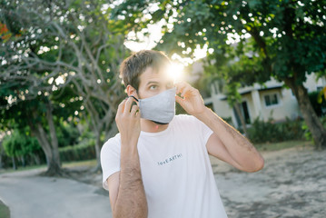 a man in a white shirt and a protective mask against a coronavirus covid-19. puts a mask on his face