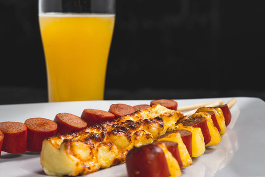 Espetinhos assados de carne, lingui&ccedil;a calabresa e queijo servido em prato no boteco com suco de laranja