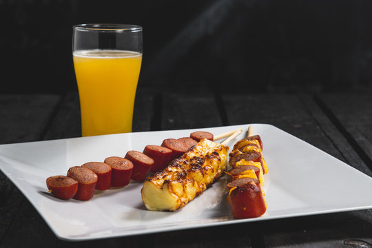 Espetinhos assados de carne, lingui&ccedil;a calabresa e queijo servido em prato no boteco com suco de laranja
