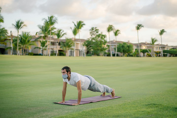 man doing yoga in a protective mask against coronavirus covid-19. In the park on green grass