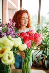 Florist at work: pretty young redhair woman making fashion modern bouquet of different flowers. .The process of creating a bouquet.