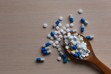 Assorted pharmaceutical medicine tablets, tablets and capsules on a wooden spoon