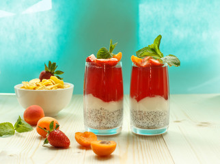 Two bright berry desserts in glasses on an aquamarine background, berries and cornflakes in the background