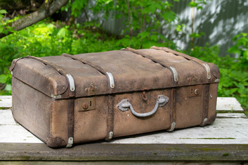 An antique brown travel suitcase with leather corners and a metal handle. 