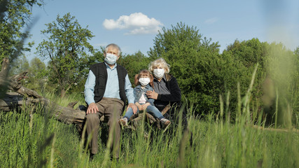 Fototapeta na wymiar Grandparents with granddaughter in medical masks in park. Coronavirus quarantine