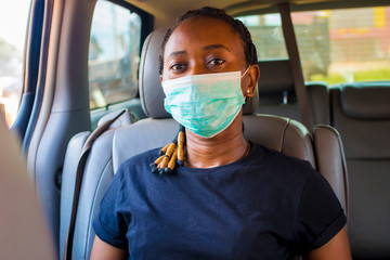 Fototapeta na wymiar young black beautiful woman sitting in a car and wearing a nose mask
