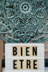 Fototapeta premium Texte Bien être sur un panneau lumineux et sculpture en bois - Décoration de salon d'esthétique