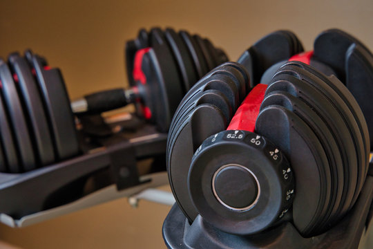 Set of adjustable dumbbells isolated on tan and brown background. Weights for working out at home.