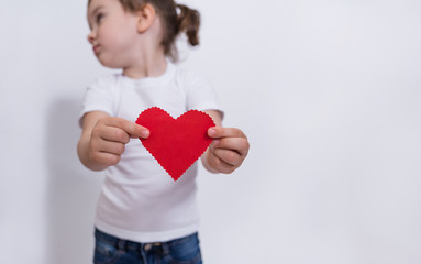 Red cardboard heart close-up on a white background with space for text. The girl holds a red heart.