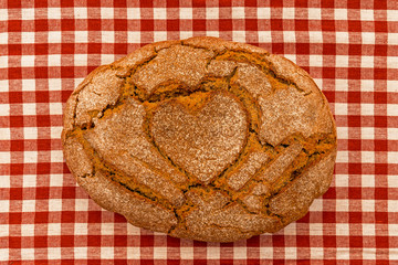 Ein Brotlaib mit einem Herz in der Mitte auf einem kariertem Tuch.