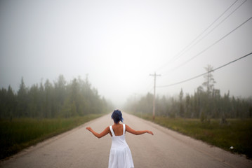 Woman in white dress and blue hair looks as if she is drifting by water surrounded by mist and fog 