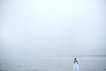 Wind blows hair of woman in white dress and blue hair looks as if she is drifting by water surrounded by mist and fog 