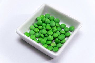 Many green pills in a white square cup
