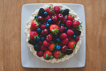 Top view at beautiful summer cake decorated with berries on white plate sitting on wooden surface.