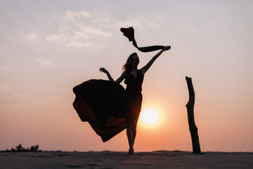 Silhouette of a girl in a red dress at sunset in the desert 