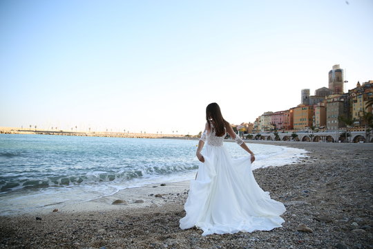 The bride in a wedding dress holds hands near the sea in Monaco.
