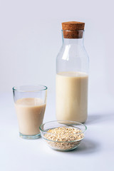A glass and bottle of non dairy oat milk on white table. Healthy food concept