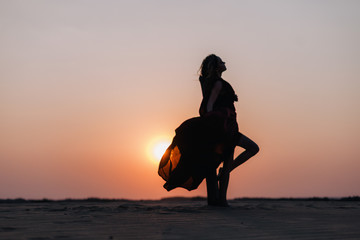 Silhouette of a girl in a red dress at sunset in the desert 