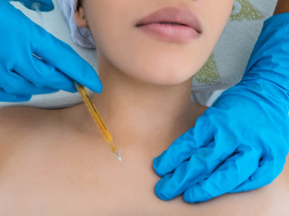 The doctor cosmetologist makes the neckline injections procedure. Young woman in a beauty salon. Cosmetology concept.