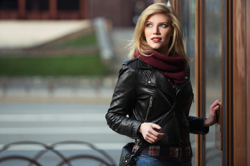Fototapeta na wymiar Young fashion blonde woman in leather jacket and snood scarf