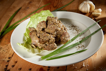 Fresh veal liver ragout in red wine sauce with onion and cram as close-up on a white plate on wooden background. Liver curry on a white plate