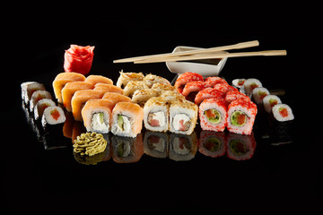 Japanese Cuisine - Appetizing Salmon Sushi Set. Philadelphia Sushi Roll - Maki Sushi with Philadelphia Cheese inside on mirror black background. Smoked salmon rolls served on a plate