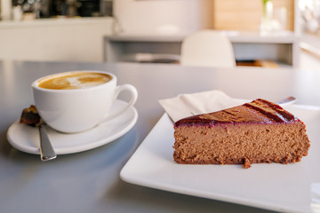 Selected focus view at simply chocolate cheese cake on white plate beside with a cup of coffee, on table beside window of bright cafe.