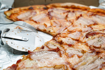 Close up on bacon and cheese pizza with two slices one quarter taken with roller cutter in empty...