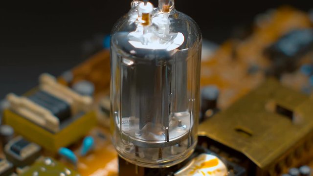 Old vacuum electronic lamp stands on a modern digital electronic board on a black background. Macro. Closeup. Shallow depth of field. Rotation