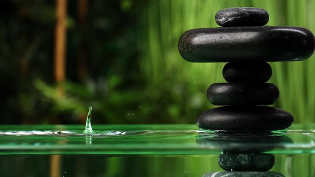 Water dripping into lake with stack of zen stones in oriental garden