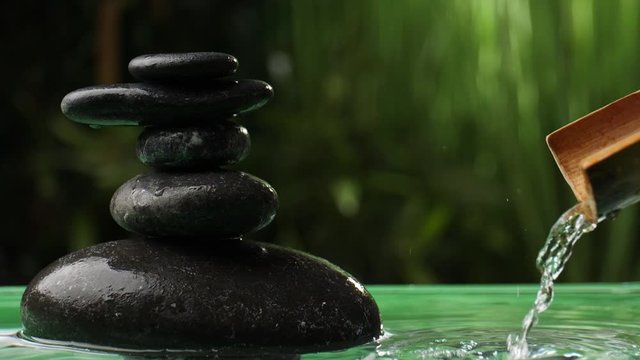 Water pouring from bamboo into lake with stack of zen stones in oriental garden