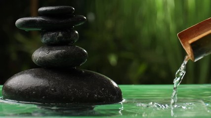 Water pouring from bamboo into lake with stack of zen stones in oriental garden
